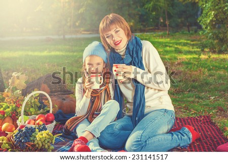 beautiful happy mother and daughter sitting on a picnic. With a cup of hot tea. Autumn harvest. Apples, pumpkins, grapes, viburnum.