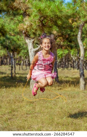 Rejoicing happy little girl jumping rope smiling full of joy and vitality in summer or spring forest.