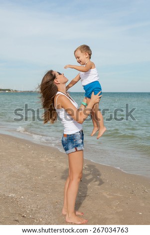 Happy family. Young mother throws up baby in the sky, on sunny day. Portrait mother and little son on the beach. Positive human emotions, feelings, emotions.