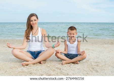 Happy family. Young happy beautiful  mother and her son doing yoga on coast of sea on beach.