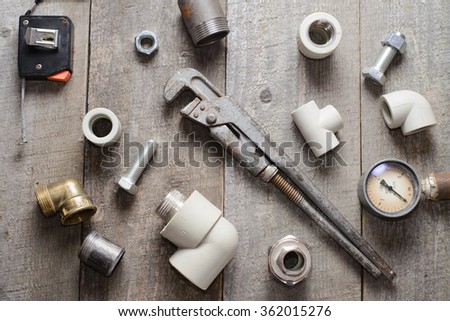 Tape-measure, internal screws, pipe wrench, pipe screw, PVC pipe connectors, manometer on old wooden table