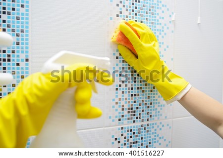 A woman washer is cleaning tiled surface in bathroom. The girl is holding a cleaning spray and a sponge in his hands. Copy space