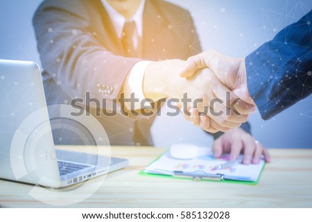 Handshake concept.two businessman shaking hands standing at the working place,laptop and digital tablet and graph financial with social network diagram and man working in the background