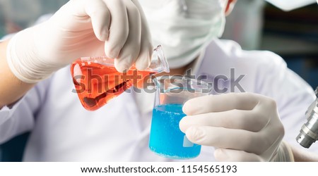 Chemist student boy pouring blue liquid in beger glass to erlenmeyer flask chemistry with red liquid on biochemical experiment. Mix water in laboratory.