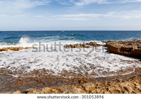 The waves beat against the rocky shore. Water flooded depressions in the rocks. Malta, Saint Julians Bay.