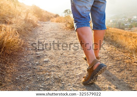 Active healthy travel - man in sports sandals climbs on the mountain. Closeup detail of male feet and stony path in sunset. Hiking in sunny day. Crimea, Russia.