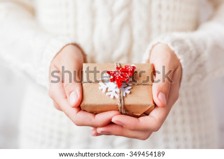 Woman in knitted sweater holding a present. Gift is packed in craft paper with white felt snowflake and red fir tree. DIY way to pack Christmas presents.