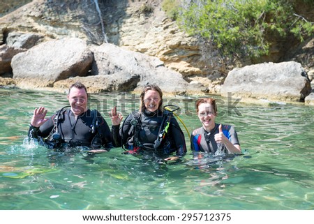 Three happy divers standing in shallow water before a dive.two of them are wearing their scuba equipment.