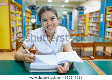 blurred library with books on the shelf, selective focus on thai young woman student in uniform is reading a book