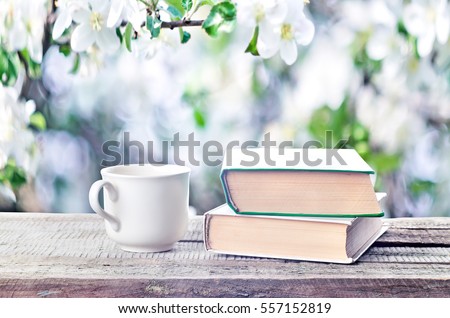 Cup hot coffee or tea, cocoa, chocolate and book outdoors on wooden table or bench in sunny weather on spring season background. Return to spring or summer time. Pile of books and cup in nature.