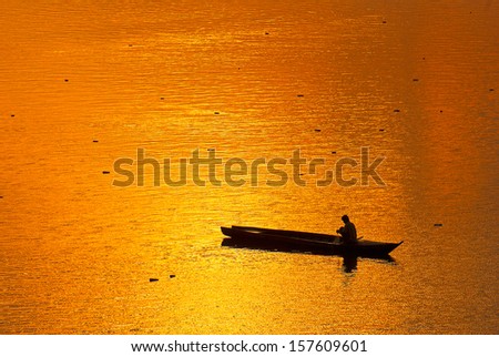 A man on the row boat in the middle of Khong river, fishing in the traditional way.