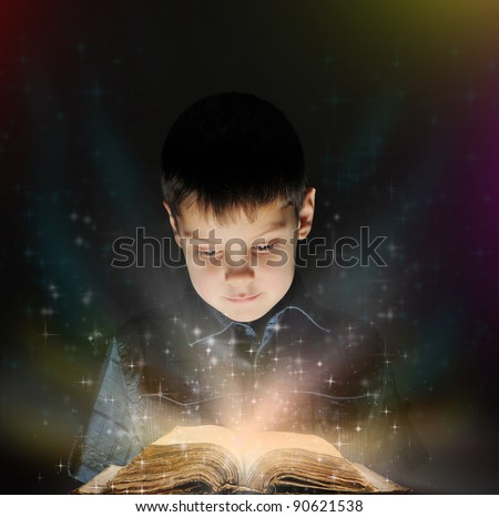 Boy is reading a magic book in the dark on a black background