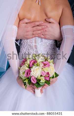 bridegroom embraces his bride, and she holds a bridal bouquet in his hands behind his back