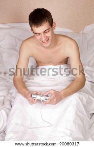 young guy having fun playing videogames in bed