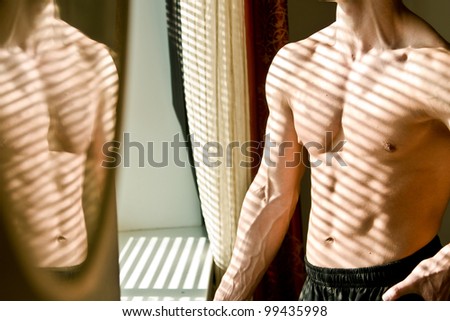 Muscular athletic man stands near the window in the morning