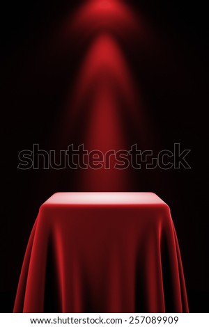 Presentation pedestal covered with a red silk cloth in front of a wall illuminated by a spot light