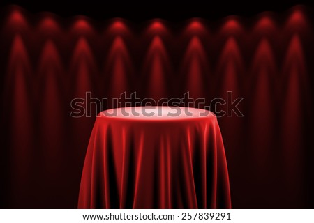 Round presentation pedestal covered with a red silk cloth in front of a wall illuminated by spot lights