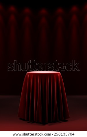 Round presentation pedestal covered with a red silk cloth in front of a wall illuminated by spot lights