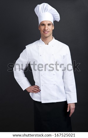 Chef cook against dark background smiling with hat hold spoon and knife
