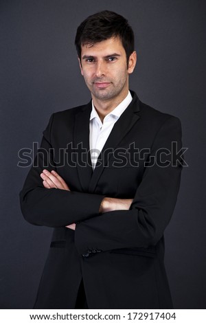 Young handsome man in black suit smiling on white background with crossed arms