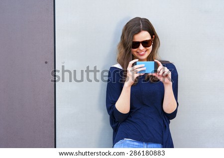 Woman taking photo with cellphone by the wall. Happy girl in city taking picture.
