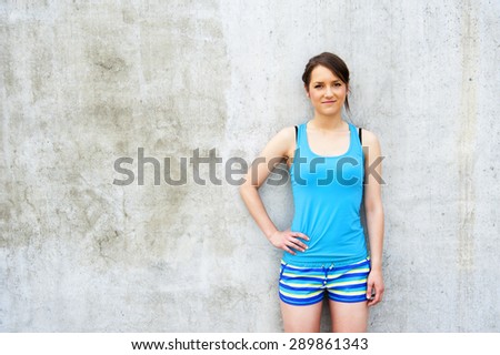 Girl in blue tank top and shorts over the wall smiling.