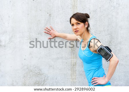 young woman resting after run by the wall in city with big smile. in blue sportswear. listing music.