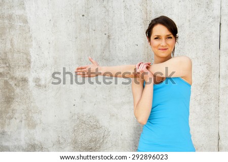 young woman stretching after run by the wall in city with big smile. in blue sportswear.