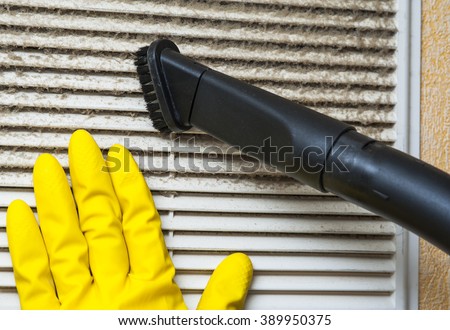Hand in yellow glove and vacuum cleaner pipe. Ventilation grill cleaning.