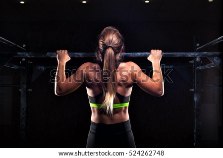 Strong fit girl in sportswear doing pull up exercise on horizontal bar. fitness workout in gym.