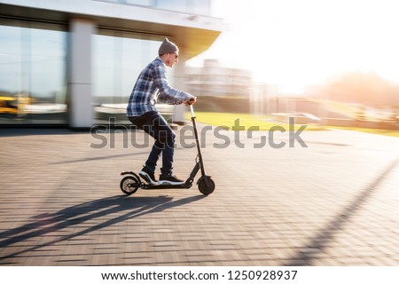 Young man in casual wear on electric kick scooter on city street in motion blur in sunday