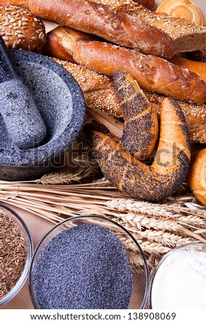 assortment of baked bread on a paper background, with spikelets of wheat, flour, poppy seeds and caraway seeds in bowls