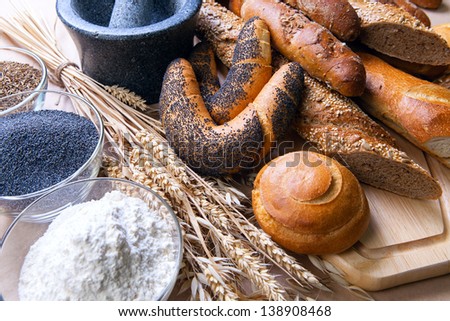 assortment of baked bread on a paper background, with spikelets of wheat, flour, poppy seeds and caraway seeds in bowls