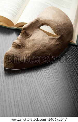 Half of the paper masks on a wooden background lies on the open book