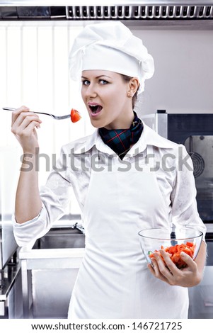 Professional female chef tries for a tasty red tomato with a fork in a professional kitchen