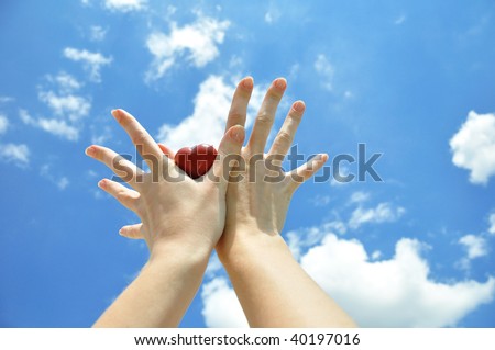 Heart in female hands against the sky