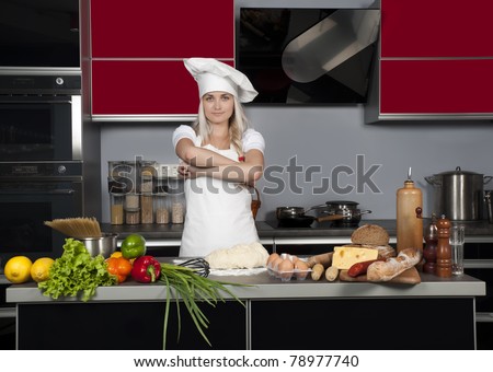 Young beautiful girl chef in the kitchen next to the kitchen table with food