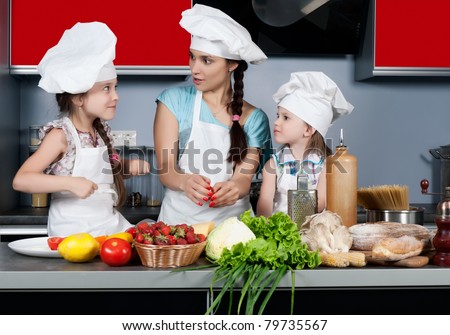 Mom teaches two daughters to cook at the kitchen table with raw food, clothing cooks