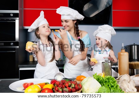 Mom teaches two daughters to cook at the kitchen table with raw food, clothing cooks