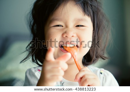 Happy Little asian girl eating yogurt and she have spoon in her mouth.