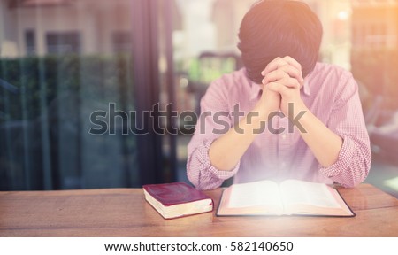 man praying on holy bible in the morning.teenager man hand with Bible praying,Hands folded in prayer on a Holy Bible in church concept for faith, spirituality and religion