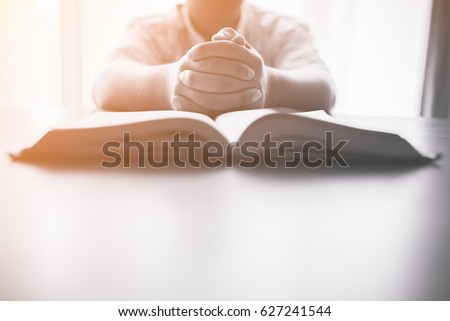 man praying on holy bible in the morning.teenager boy hand with Bible praying,Hands folded in prayer on a Holy Bible in church concept for faith, spirituality and religion