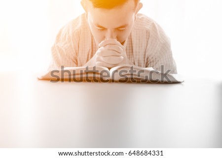 man praying on holy bible in the morning.teenager boy hand with Bible praying,Hands folded in prayer on a Holy Bible in church concept for faith, spirituality and religion.