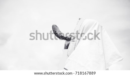 Jewish man in Tallit blowing the Shofar (horn) of Rosh Hashanah (New Year Jew) on sunset sky.Religious and Holidays symbol concept.Black and white.vintage tone.