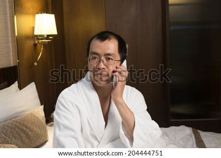 Mature Asian man in bathrobe in hotel, using cellphone.