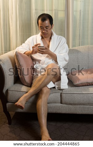 Mature Asian man in bathrobe in hotel, using cellphone.