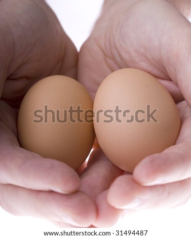 Two hands holding two eggs surrounded with feathers making a nest