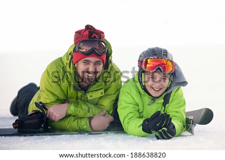 father and son in ski suits lie on the snow