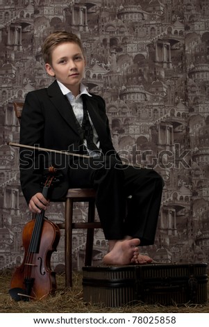 The tired boy in a classical suit sits on a chair with a violin in hands
