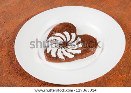 Brown heart shaped cookie with sugar powder on white plate